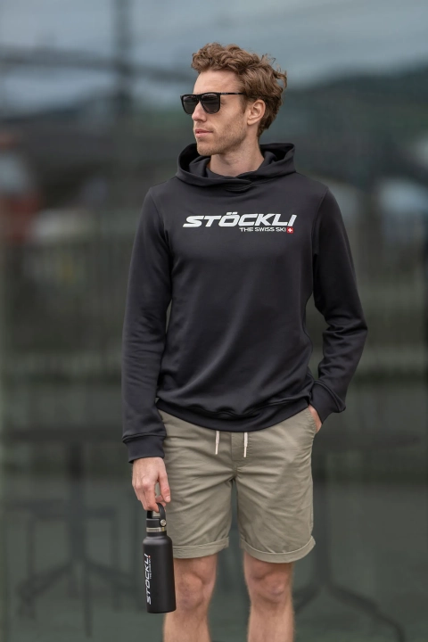 Model ma na sobie bluzę Stöckli HOODY THE SWISS SKI BLACK, prezentując krój Regular Fit.