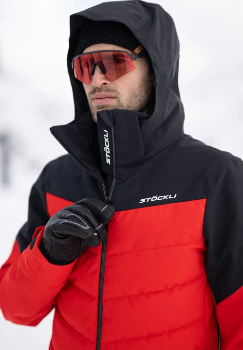 Zbliżenie na modela w kurtce STOECKLI SKI JACKET RACE i kominie Stöckli, widoczne detale.