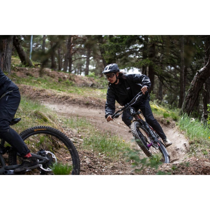 Rowerzysta w czarnym matowym kasku MTB Alpina Taunus MIPS podczas dynamicznej jazdy na rowerze górskim po leśnym szlaku.